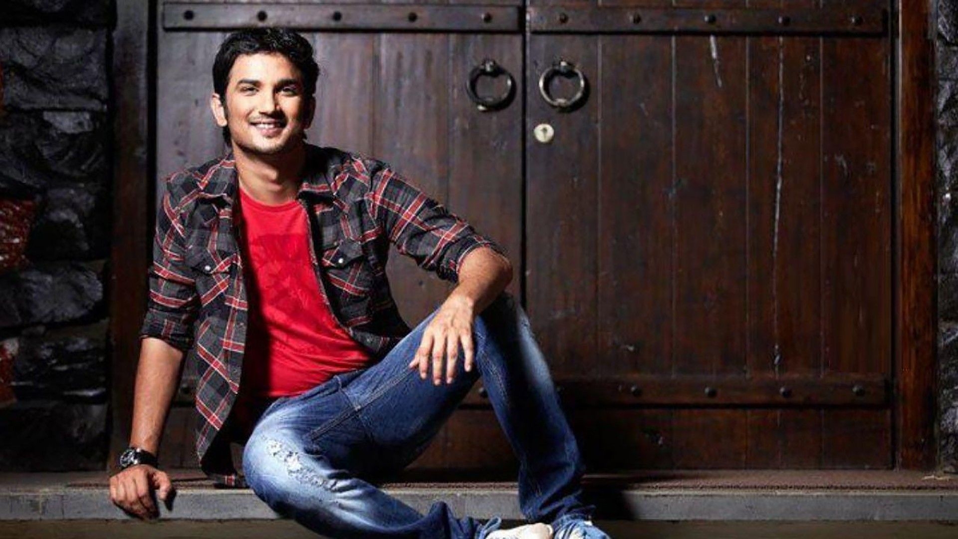 1920x1080 Sushant Is Sitting On Floor Wearing Red Black Shirt And Blue Jean In Wooden Door Background HD Sushant Singh Rajput Wallpaper, Desktop